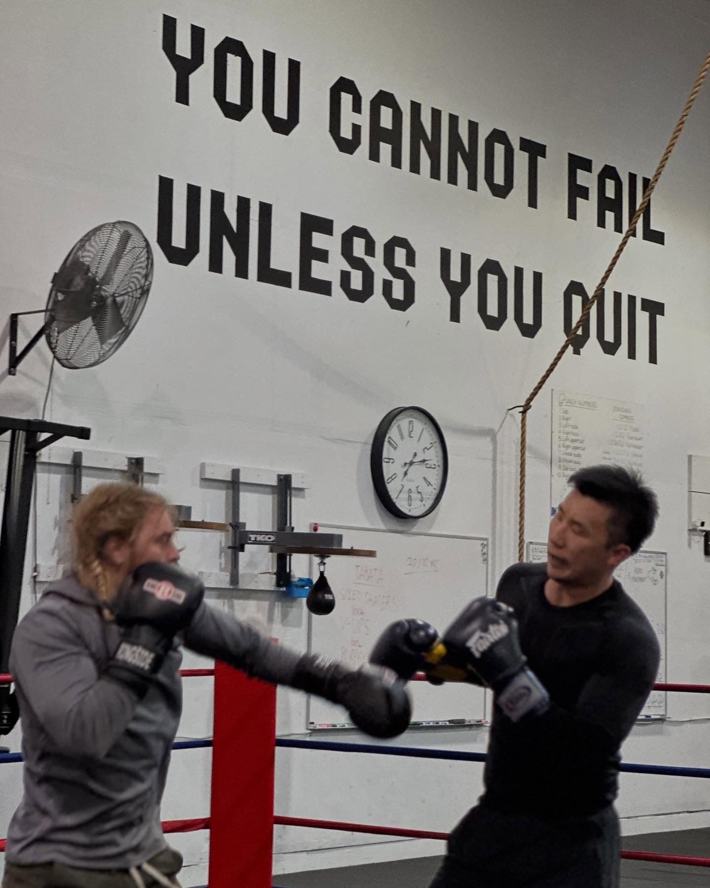Two members sparring beneath the YOU CANNOT FAIL UNLESS YOU QUIT wall at Ballard Barbell and Boxing Club